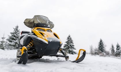Gul og svart snøscooter uten fører står parkert i snøkledd landskap